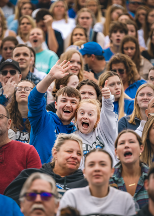 Two fans wave to the camera from the stands