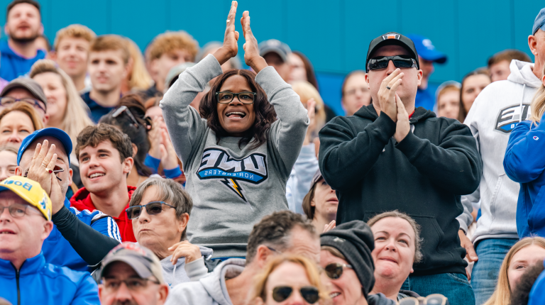 A woman in a UNE sweatshirt claps for the football team