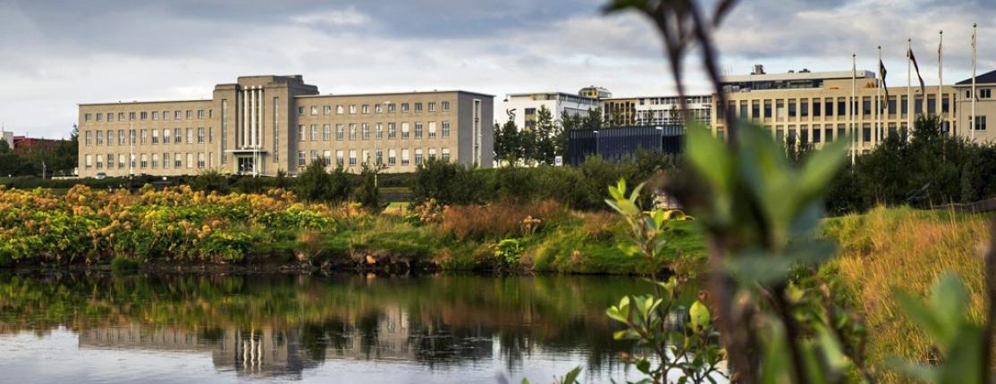 A scenic view of a large building with a pond in the foreground and greenery around, 在多云的天空衬托下